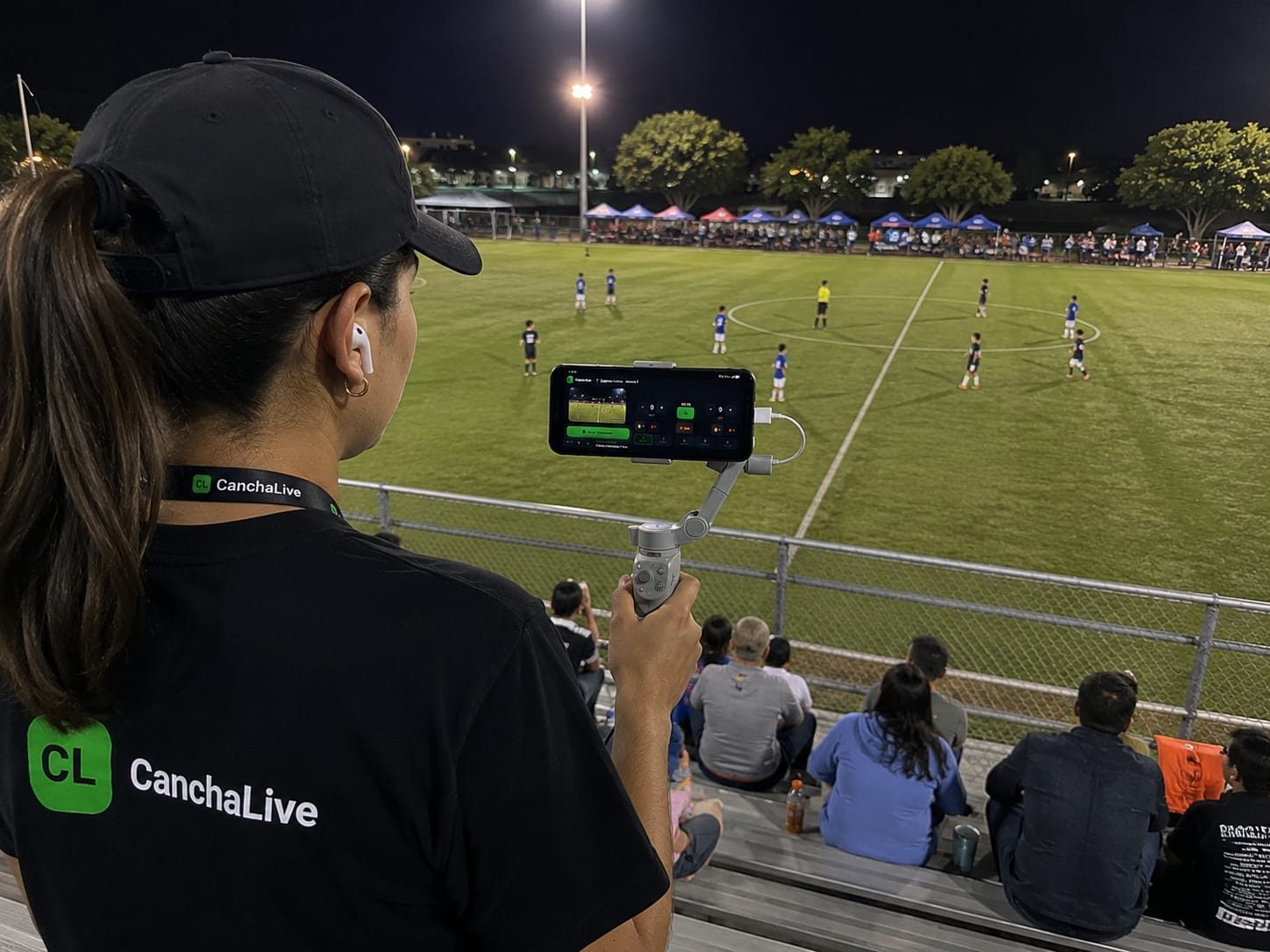 Persona con playera y credencial de CanchaLive transmitiendo en un estadio